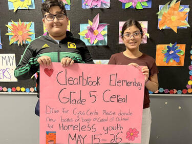 Two elementary students stand holding a poster about the Cereal Drive