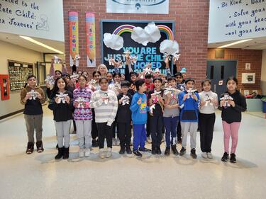 Group of elementary students standing in front foyer of school, showing of art project they completed