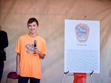 Indigenous Youth stands on stage, acknowledged for their design for APD shoulder flash.