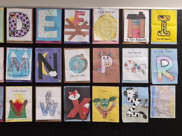 Student-created alphabet artwork displayed on a classroom bulletin board, featuring decorative letters A to Z made from drawings and crafts representing words or objects associated with each letter.