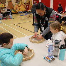 A female ISW helps two female grade 5 students with their drums