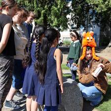 Female secondary student reads book inspired by elementary student artwork as others listen